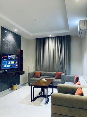 A modern living room with a flat-screen TV, a sofa, a coffee table, and a large window with curtains. - Calm Apartment Serviced (Riyadh)