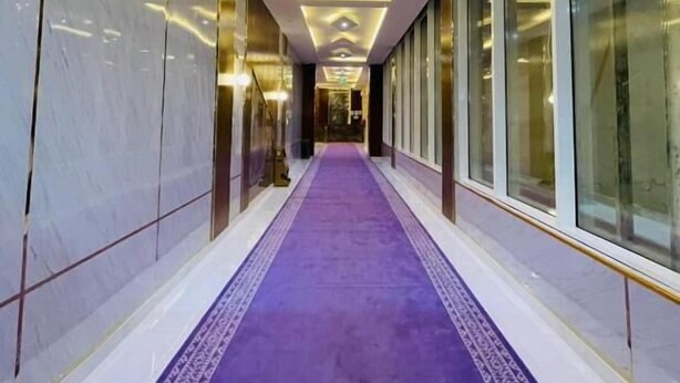 Un pasillo con alfombra morada, paredes de mármol e iluminación empotrada.