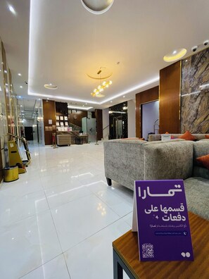 A modern hotel lobby with a reception desk, a sofa, and a sign with Arabic text.