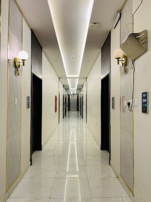 A long, well-lit hallway with a reflective floor, doors on either side, and a ceiling light fixture. - Calm Apartment Serviced (Riyadh)