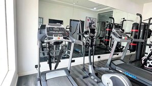 Un gimnasio con máquinas de cardio, equipo de pesas y un espejo grande.
