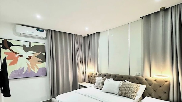 Un dormitorio moderno con una cama grande, una mesita de noche, un equipo de aire acondicionado, una obra de arte en la pared y un armario.