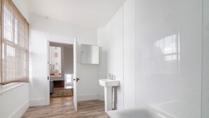 A modern bathroom with a wooden floor, a white bathtub, and a wall-mounted sink. - Spacious apartment in London (London)