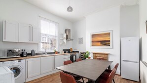 A modern kitchen with white cabinets, a dining table, and a refrigerator. - Spacious apartment in London (London)