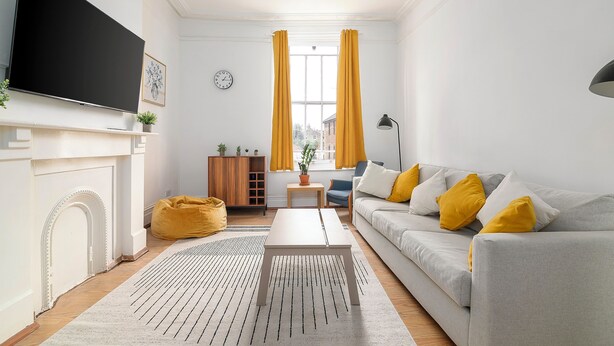 A living room with a flat-screen TV, a sofa with yellow cushions, a coffee table, a fireplace, and a window with curtains. - Spacious apartment in London (London)