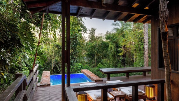 Una terraza de madera con piscina, sillones de descanso y una mesa.