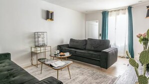 Una sala moderna con un sofá gris oscuro, una mesa de centro de vidrio y una mesita auxiliar con un marco de foto y una taza.