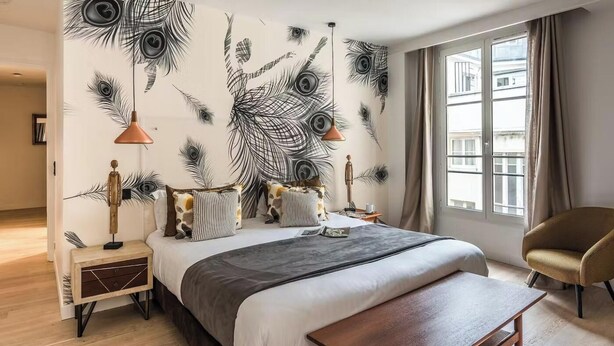 Un dormitorio con una cama grande, una mesita de noche, un banco, una silla y una pared decorada con un diseño de pluma de pavo real.