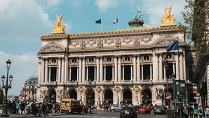 Un edificio histórico y majestuoso con arquitectura ornamentada, amplias ventanas en arco y estatuas en el techo.
