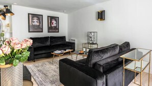 Una sala de estar moderna con un sofá negro, una mesa de centro de vidrio y un jarrón decorativo con flores.