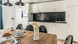 Una cocina moderna con armarios blancos, salpicadero negro y una mesa de comedor con sillas.