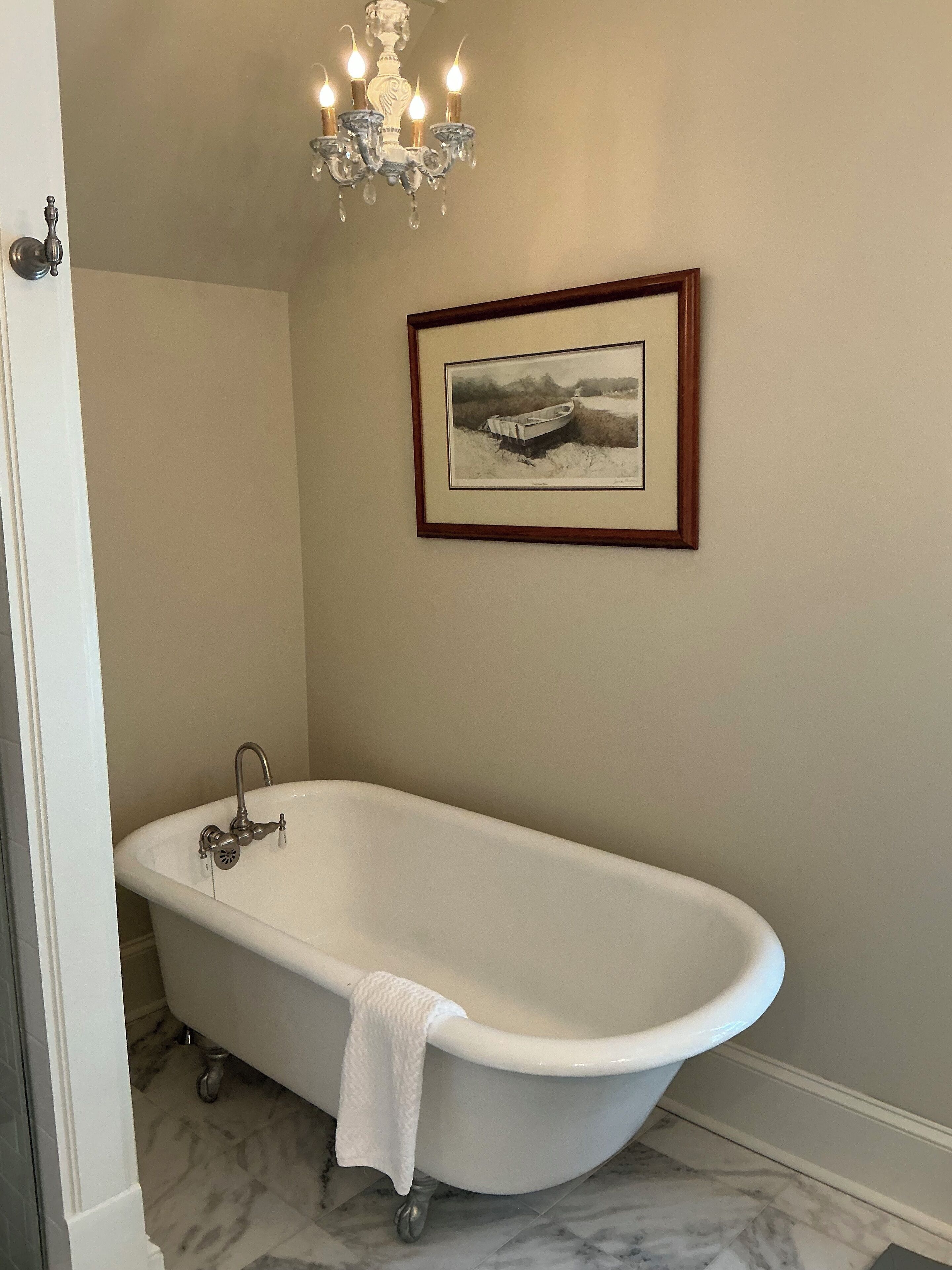 A bathroom with a freestanding bathtub, a chandelier, and a framed photograph on the wall.