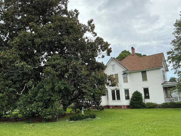 A white two-story house with a red roof, surrounded by a well-maintained lawn and large trees. - Magnolia House Bed & Breakfast (Oriental)