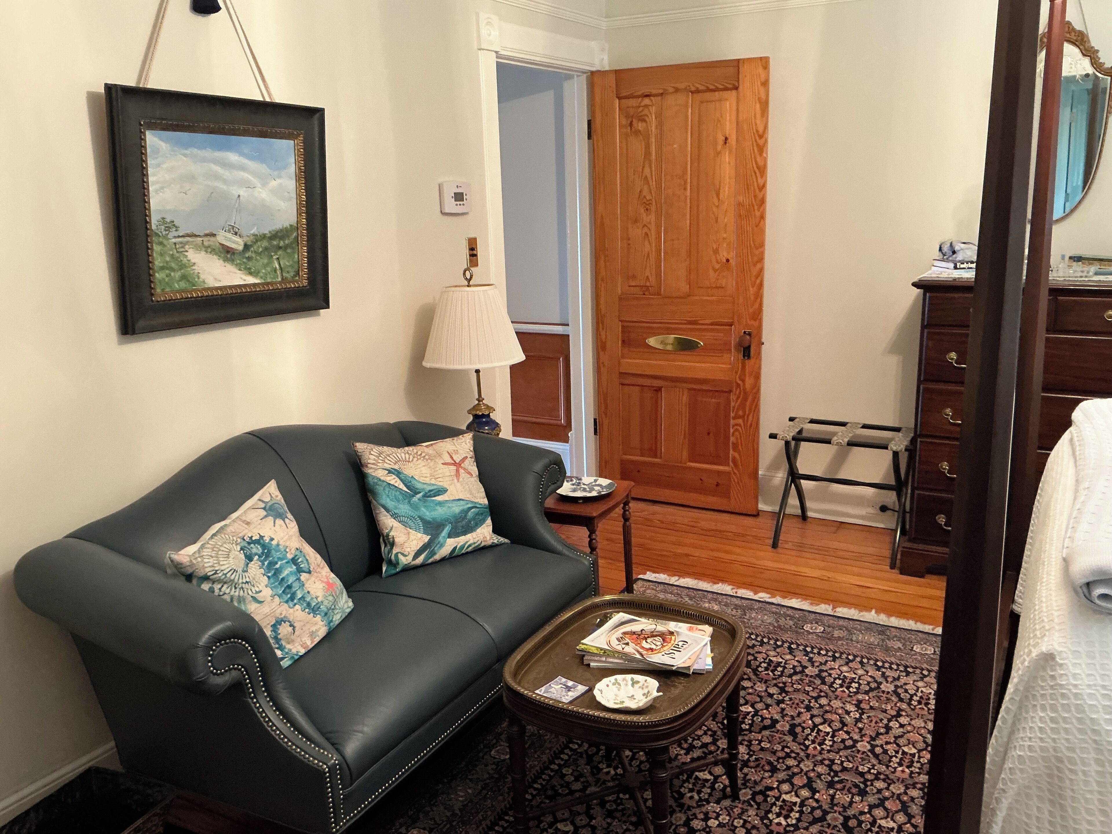 A living room with a dark leather sofa, a small table with a tray, a lamp, and a door leading to another room.
