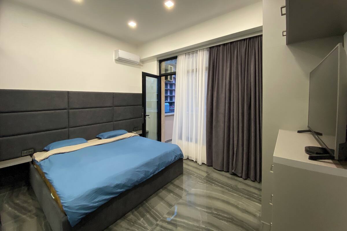 Una habitación de hotel moderna con una cama grande, un televisor de pantalla plana y un balcón con cortinas.