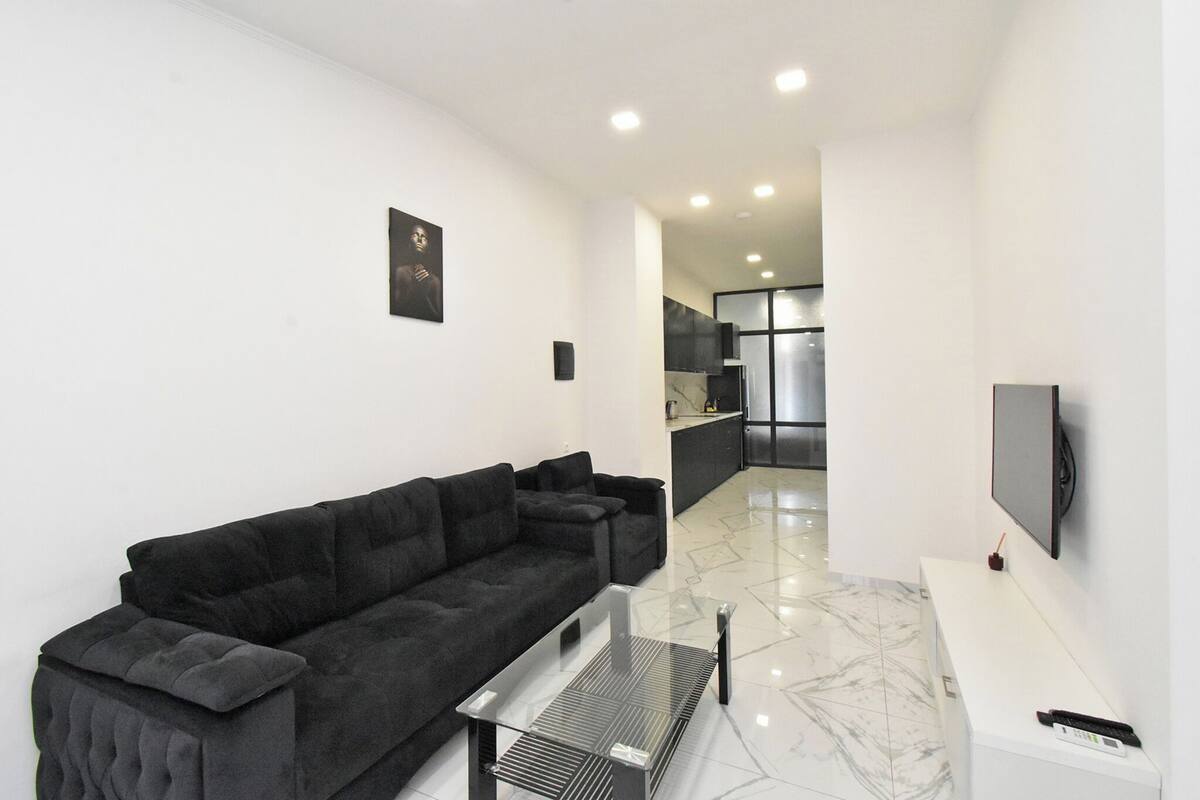 Una sala de estar moderna con un sofá negro, una mesa de centro y un televisor de pantalla plana montado en la pared.