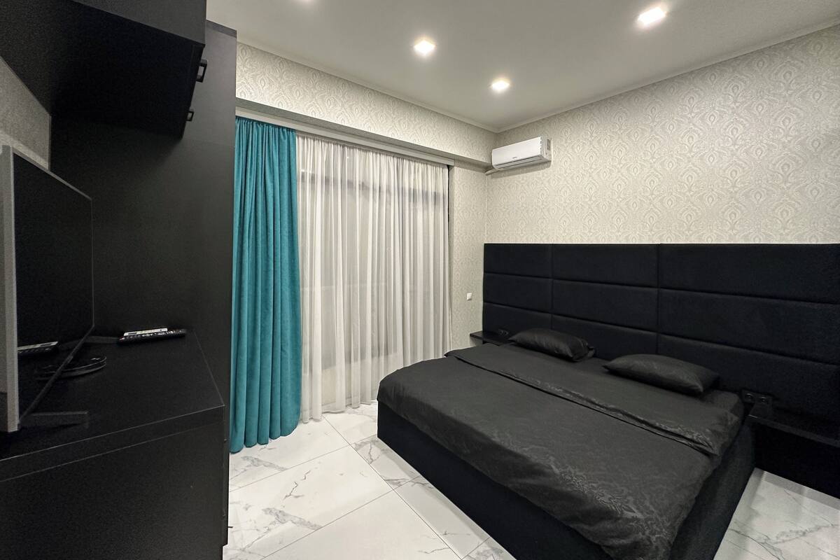 Un dormitorio moderno con una cama grande, un televisor y una ventana con cortinas.