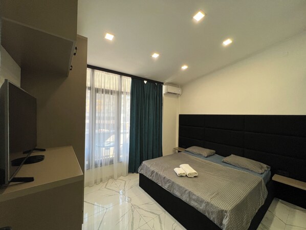 A modern hotel room with a large bed, a TV, and an air conditioning unit.