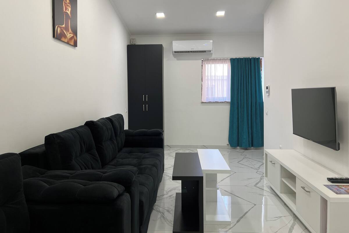 Una sala de estar moderna con un sofá negro, una mesa de centro blanca, un televisor de pantalla plana y un mueble negro.