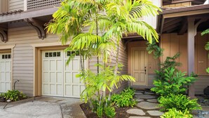 A house with a garage, a covered porch, and a garden with palm trees and shrubs.