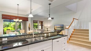 A kitchen with a granite countertop, white cabinets, and a built-in sink. There is a dining area with a table and chairs, and a staircase with a wooden railing.