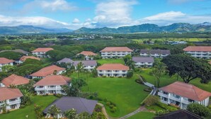 A residential area with multiple houses, each with a red roof and white exterior walls, surrounded by lush greenery and a mountainous backdrop. - Summer Deal Top Floor Poipu Condo Steps from Beach with Resort Pool (Koloa)