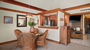 A dining area with wicker chairs, a wooden table, and a hanging pendant light. - Summer Deal Top Floor Poipu Condo Steps from Beach with Resort Pool (Koloa)