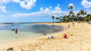 A beach with clear blue water, sandy shore, and palm trees. - Summer Deal Top Floor Poipu Condo Steps from Beach with Resort Pool (Koloa)