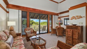 A spacious living room with a large sliding glass door leading to a balcony, wicker furniture, and a wooden cabinet. - Summer Deal Top Floor Poipu Condo Steps from Beach with Resort Pool (Koloa)