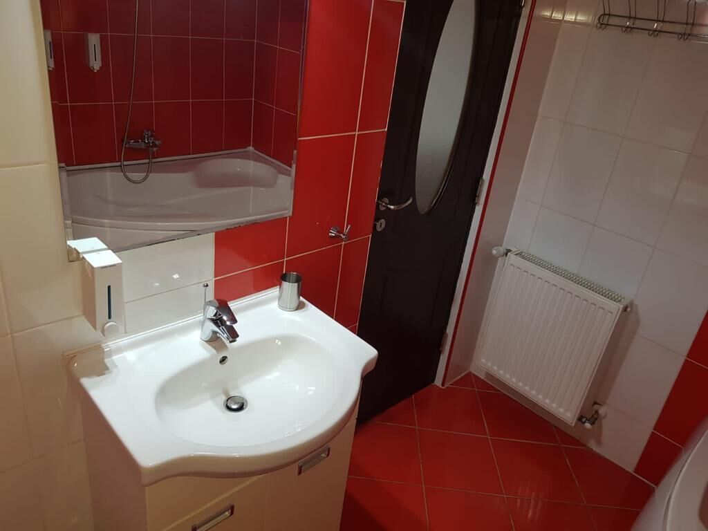 Casa de banho com uma pia branca, azulejos vermelhos, uma porta preta e um radiador branco.