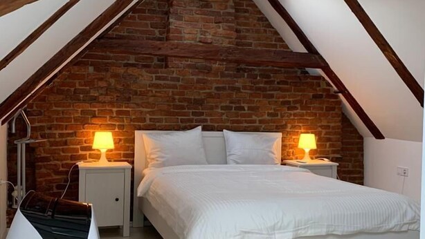 Een slaapkamer met een schuine daklijn, zichtbare houten balken, een bakstenen muur en een dakvenster.