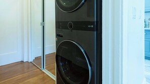 A laundry room with a black wall-mounted washer and dryer, wooden flooring, and a white door leading to another room. - Beautiful Turn of the Century Home with Pet Friendly Yard (Martinez)