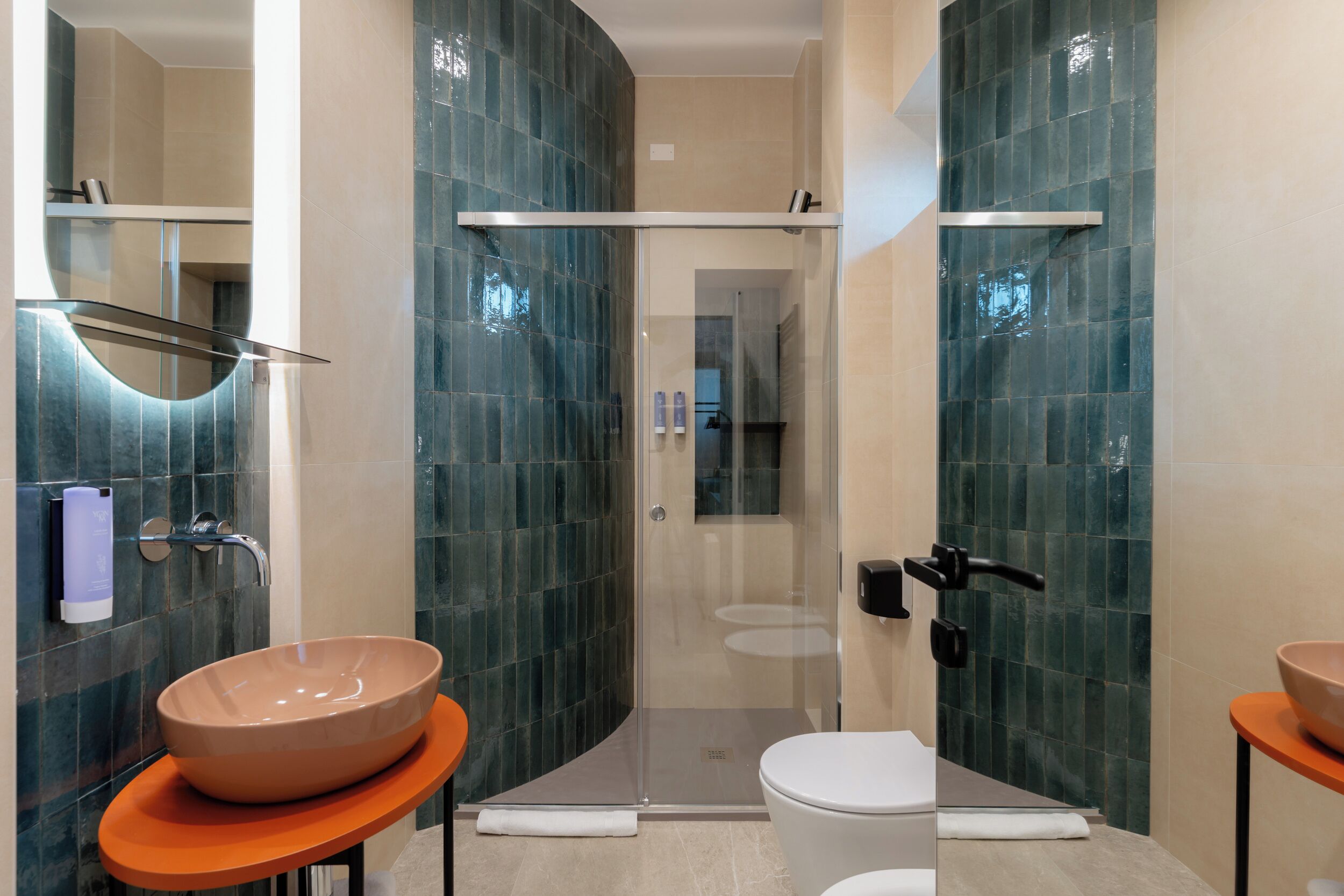 A modern bathroom with a glass shower enclosure, two sinks with orange countertops, and a white toilet.