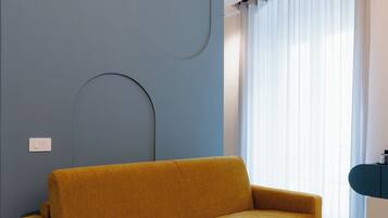 A modern living room with a mustard-colored sofa, a curved wall design, and a large window with sheer curtains.