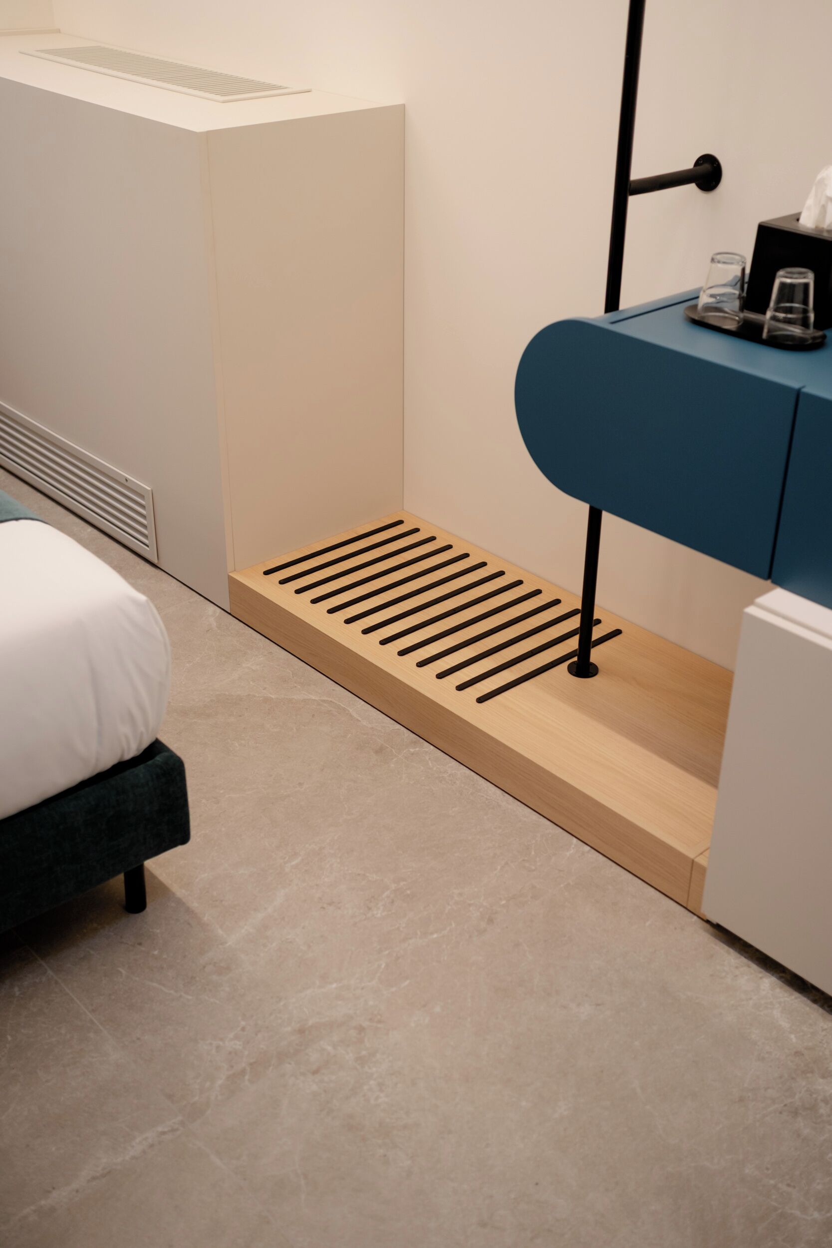 A modern hotel room with a bed, a blue cabinet, a wooden slatted bench, and a white radiator.