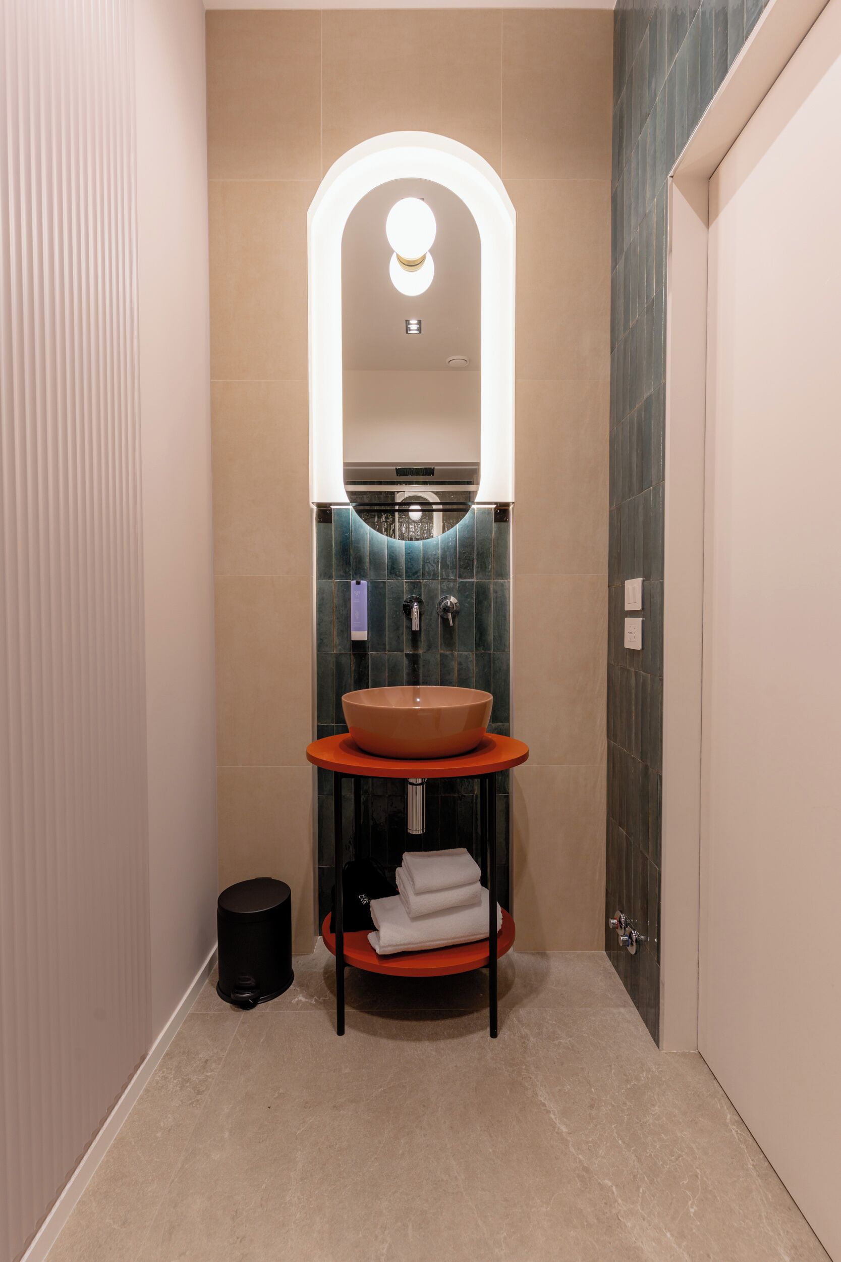 Een moderne badkamer met een rond wastafel, een spiegel met ingebouwde verlichting en een handdoekhouder.