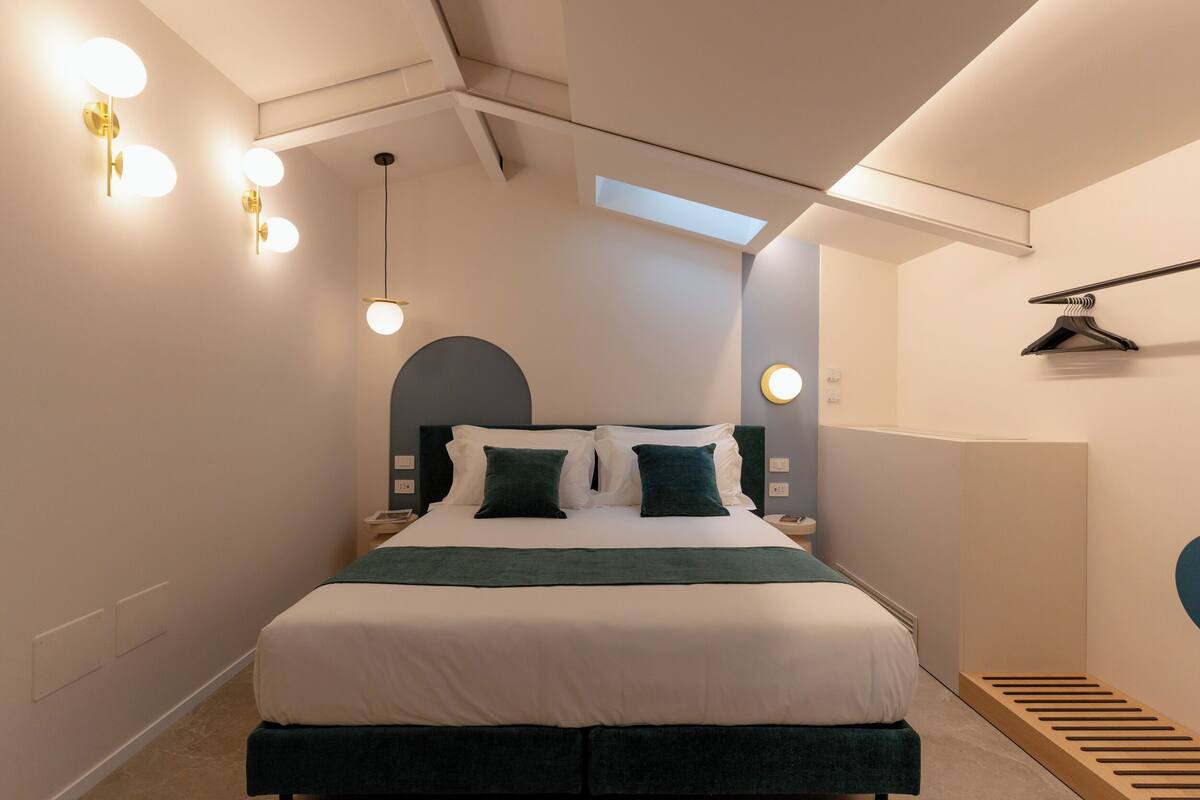 Un dormitorio moderno con una cama grande, mesitas de noche, una lámpara colgante y un tragaluz.