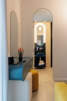 A modern bathroom with a blue vanity, a large mirror, and a blue sink. There is a yellow ottoman and a potted plant with red leaves.