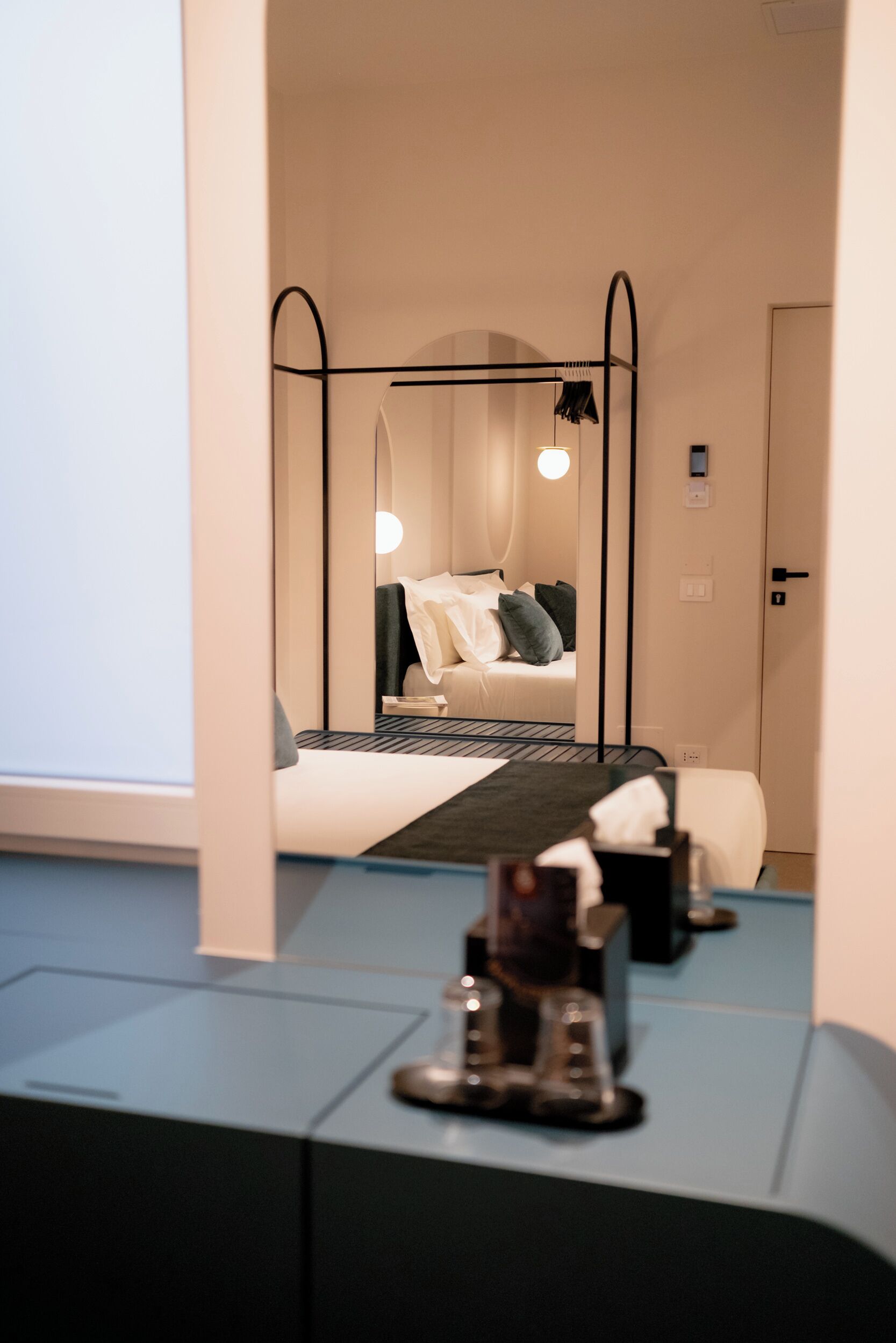 A modern hotel room with a bed, bedside table, and a mirror reflecting the room.