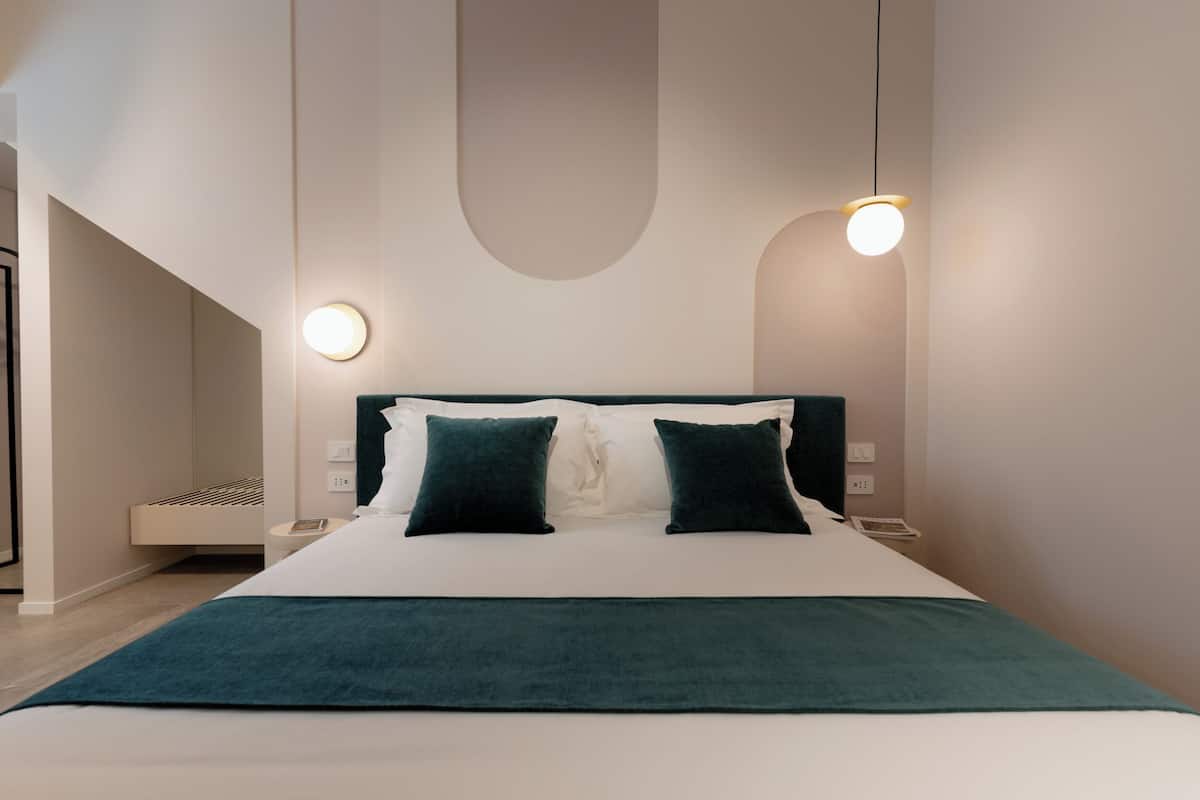 Una habitación de hotel moderna con una cama grande, dos mesitas de noche y una lámpara fijada a la pared.