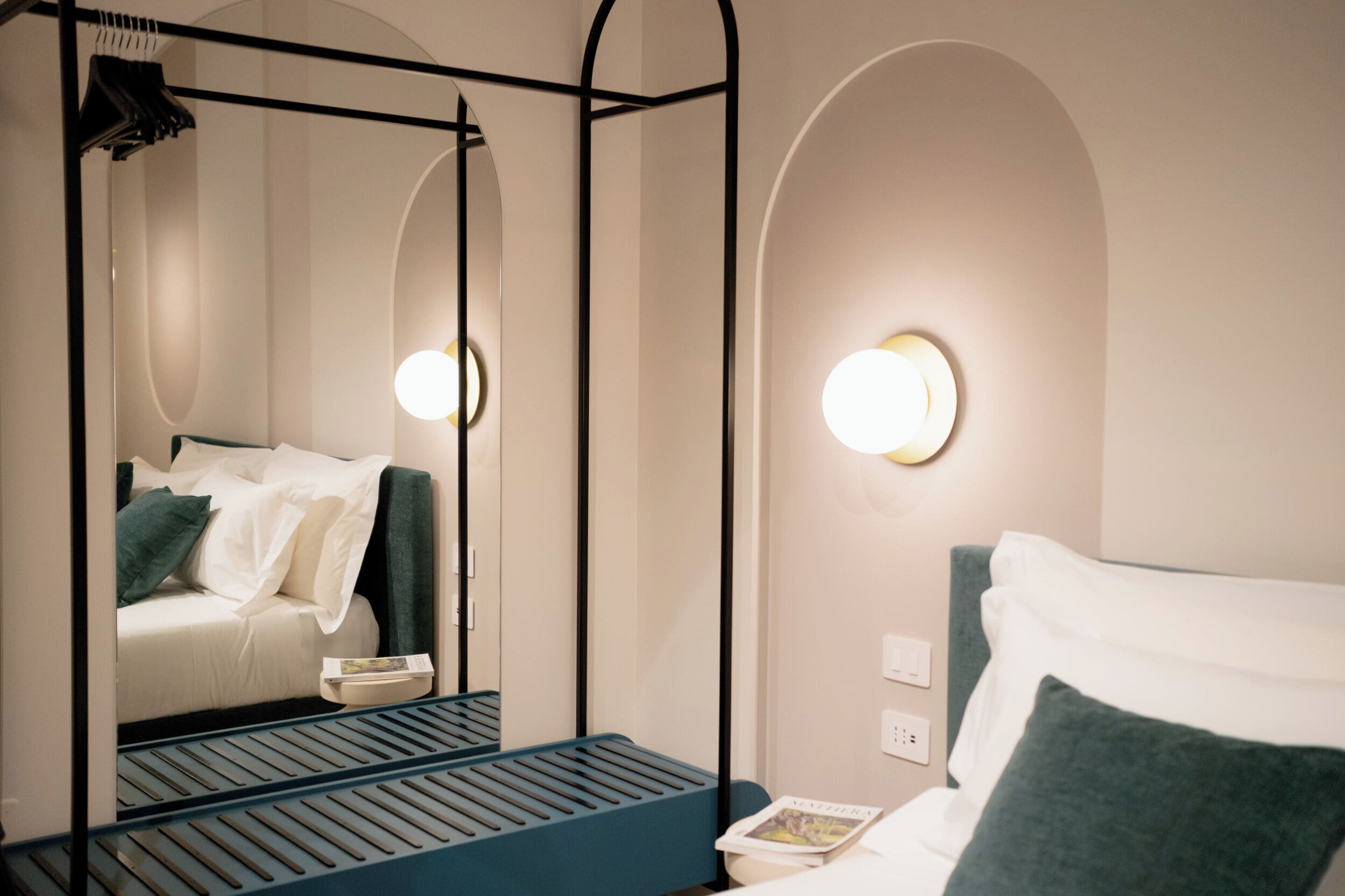 Ein Hotelzimmer mit einem Himmelbett, einem Nachttisch mit einem Buch, einem Spiegel und einer Wandleuchte.
