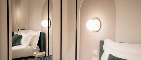 Une chambre d’hôtel avec un lit à baldaquin, une table de chevet avec un livre, un miroir et un luminaire fixé au mur.