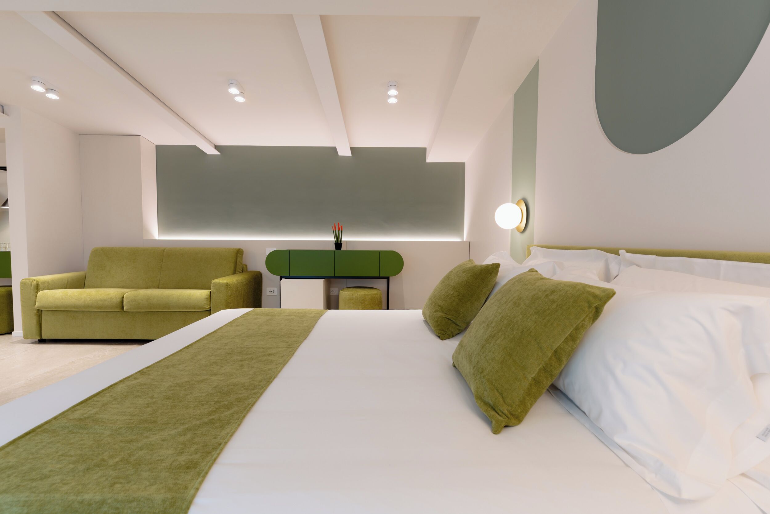 A modern hotel room with a large bed, green sofa, and a desk.