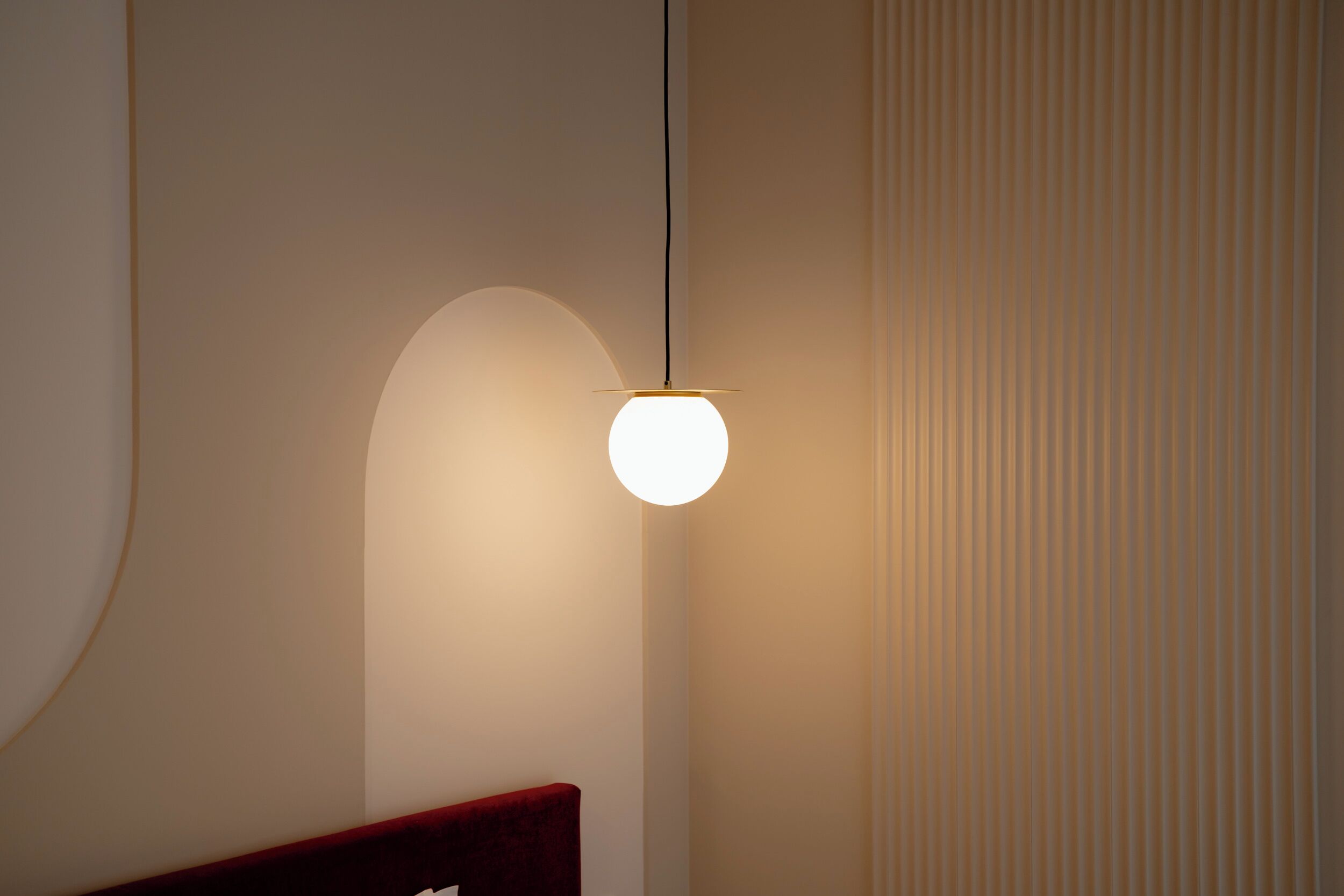 A modern room with a unique curved wall design, a hanging light fixture, and a textured wall panel.