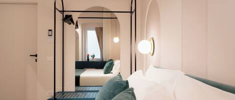 Une chambre d’hôtel avec un lit, un miroir, un luminaire suspendu et une vue sur une autre chambre, visible à travers une porte en arc de cercle.