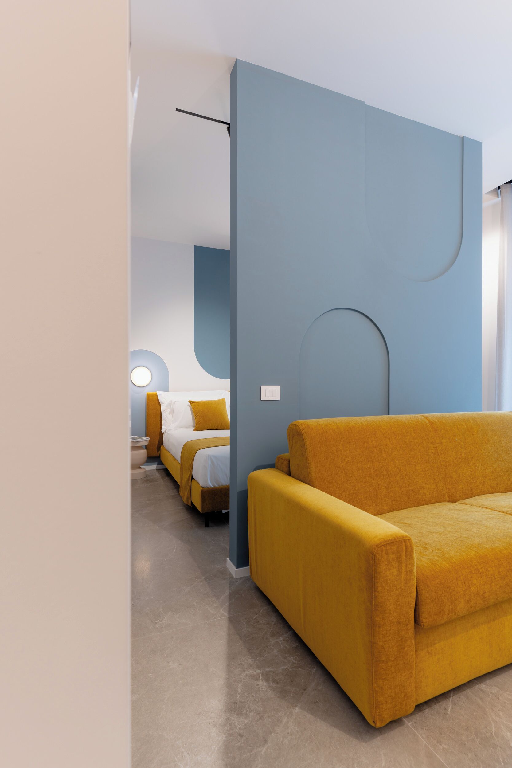 A modern hotel room with a sofa, a bed, and a nightstand.