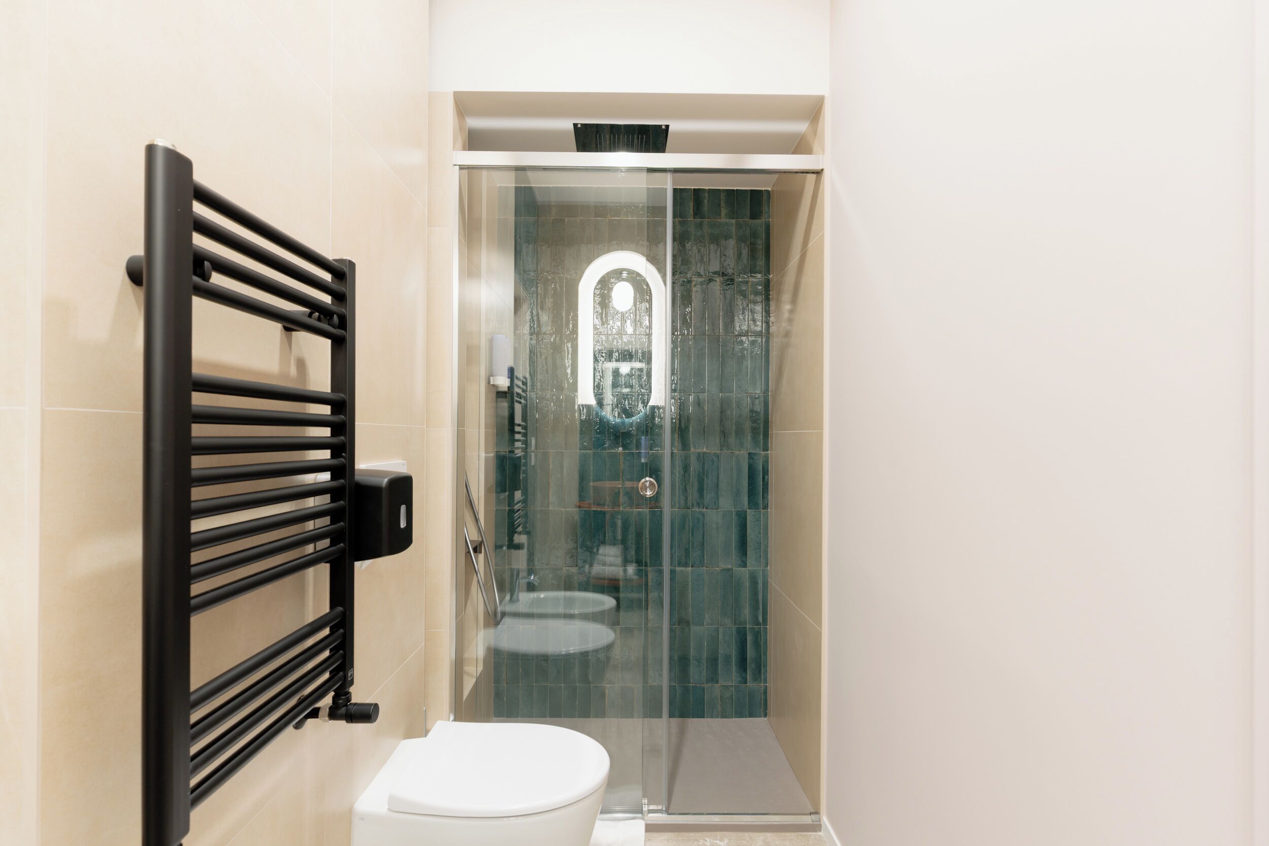 Un baño moderno con cabina de ducha de vidrio, un perchero negro y un inodoro blanco.