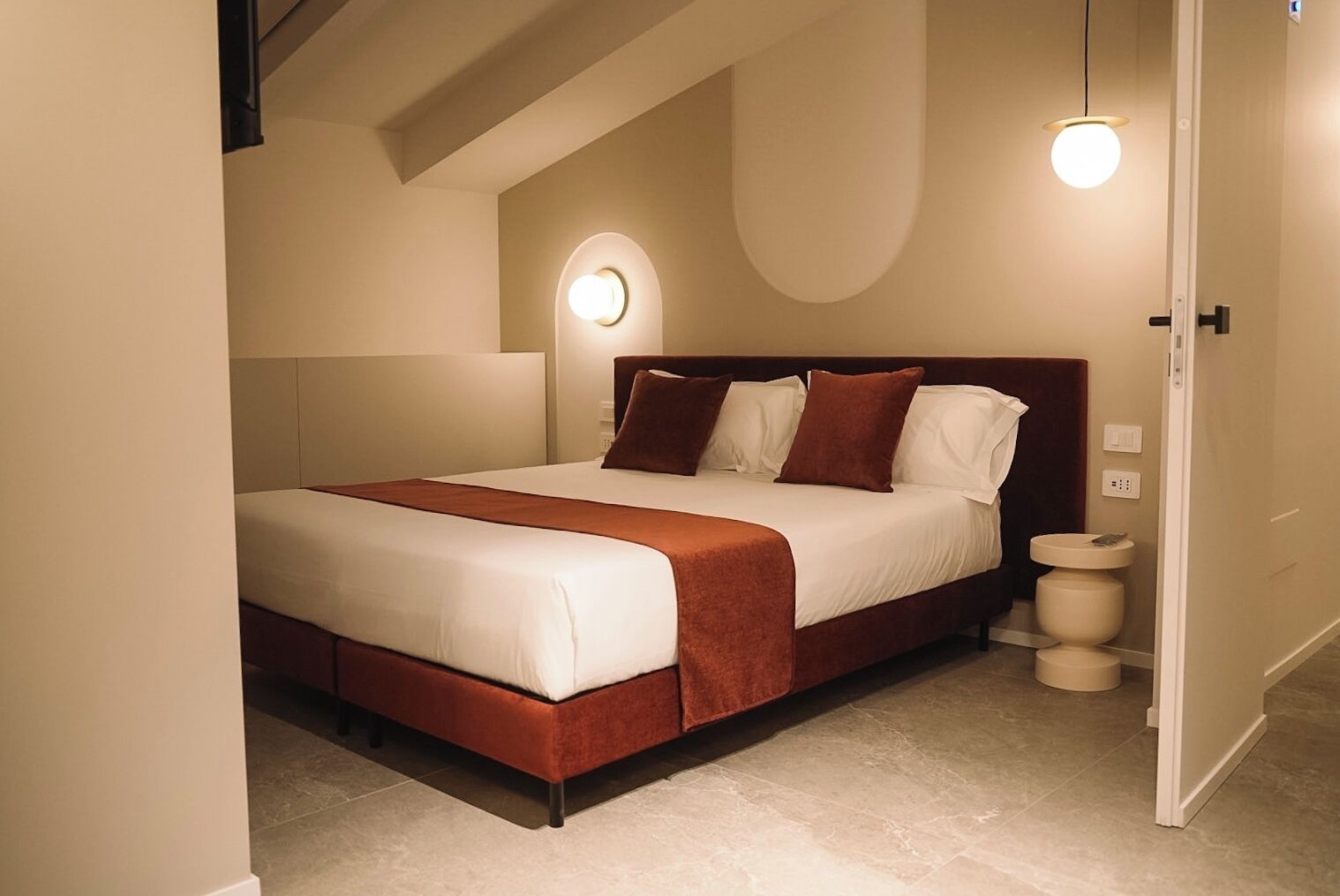 A bedroom with a bed, bedside tables, and a wall-mounted light fixture.