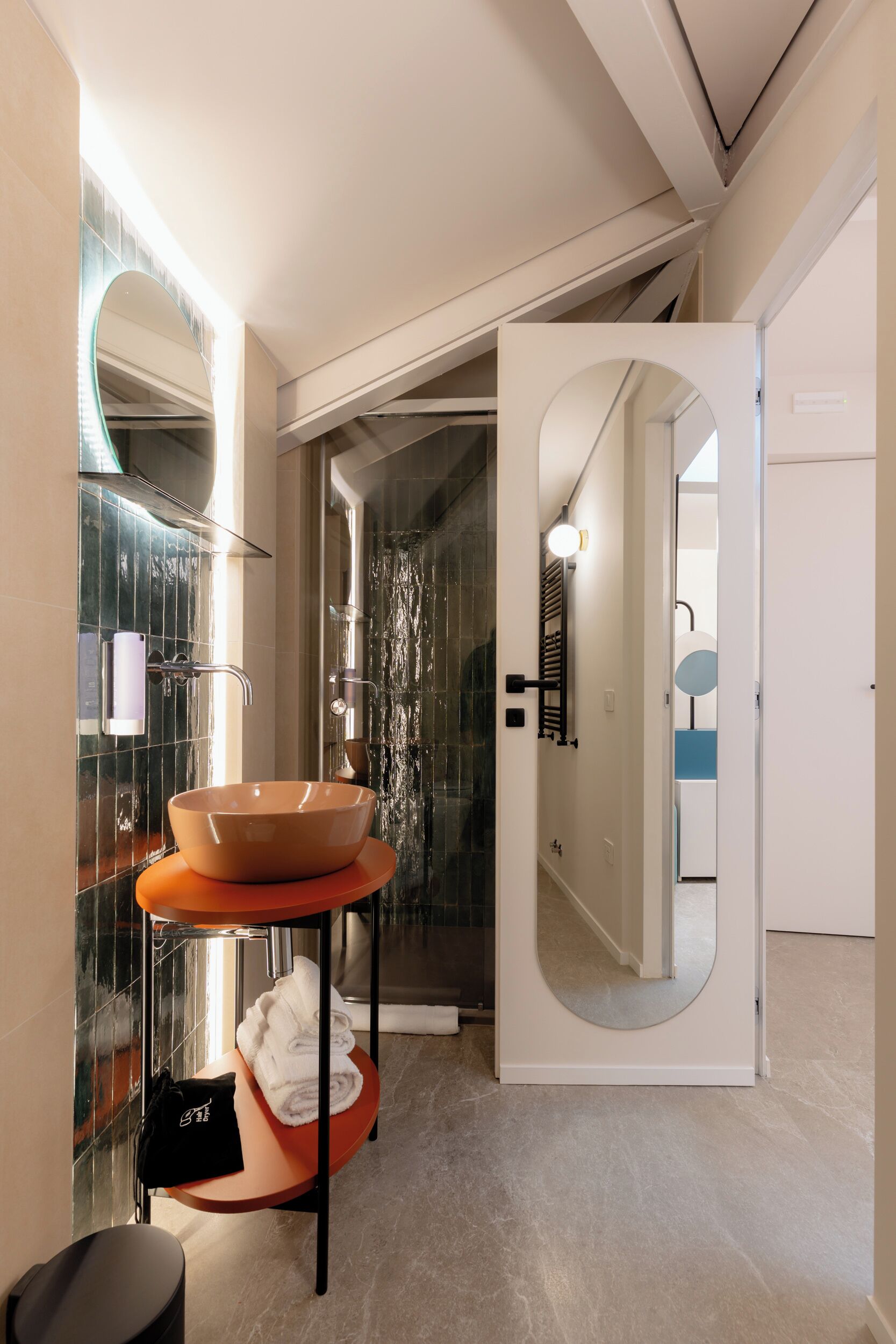 Une salle de bain moderne avec un grand lavabo ovale, une douche en verre et un miroir doté d’un cadre circulaire.
