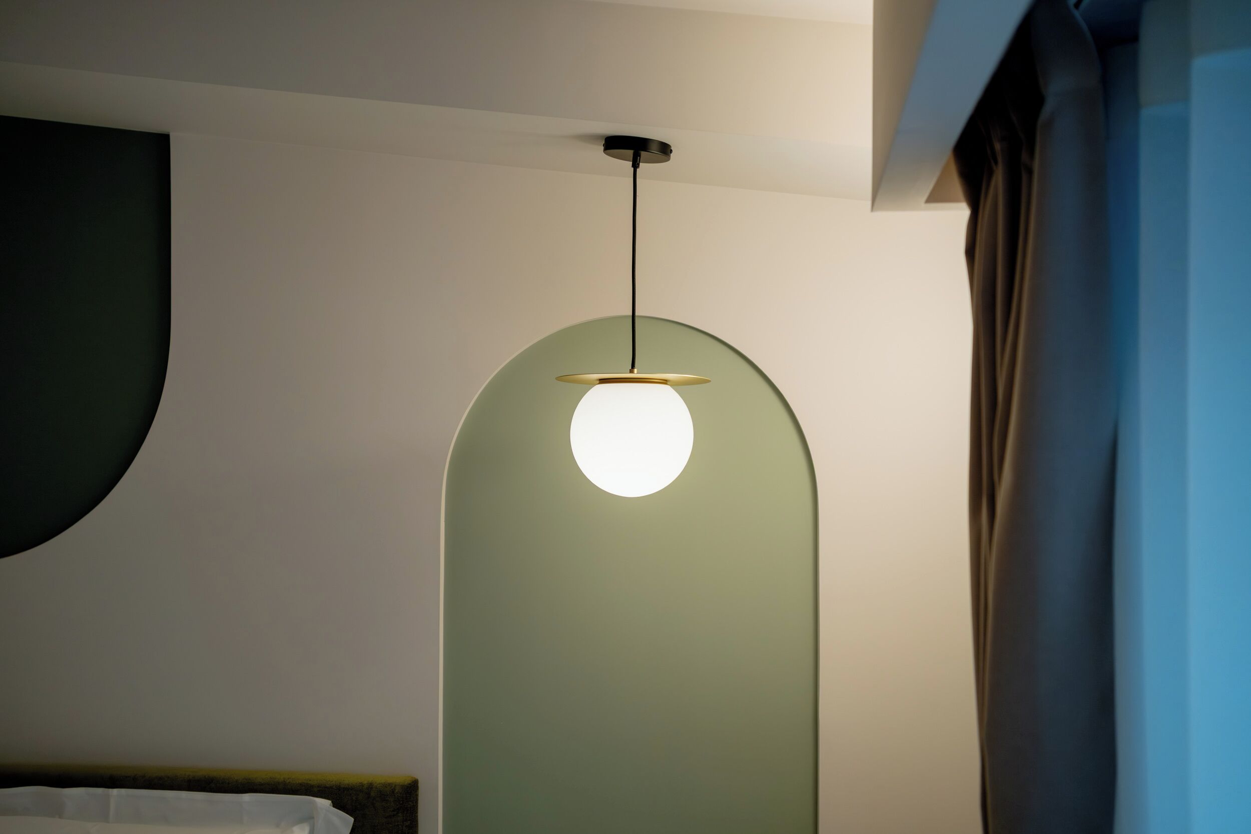 A room with a bed, a green wall, and a hanging light fixture.